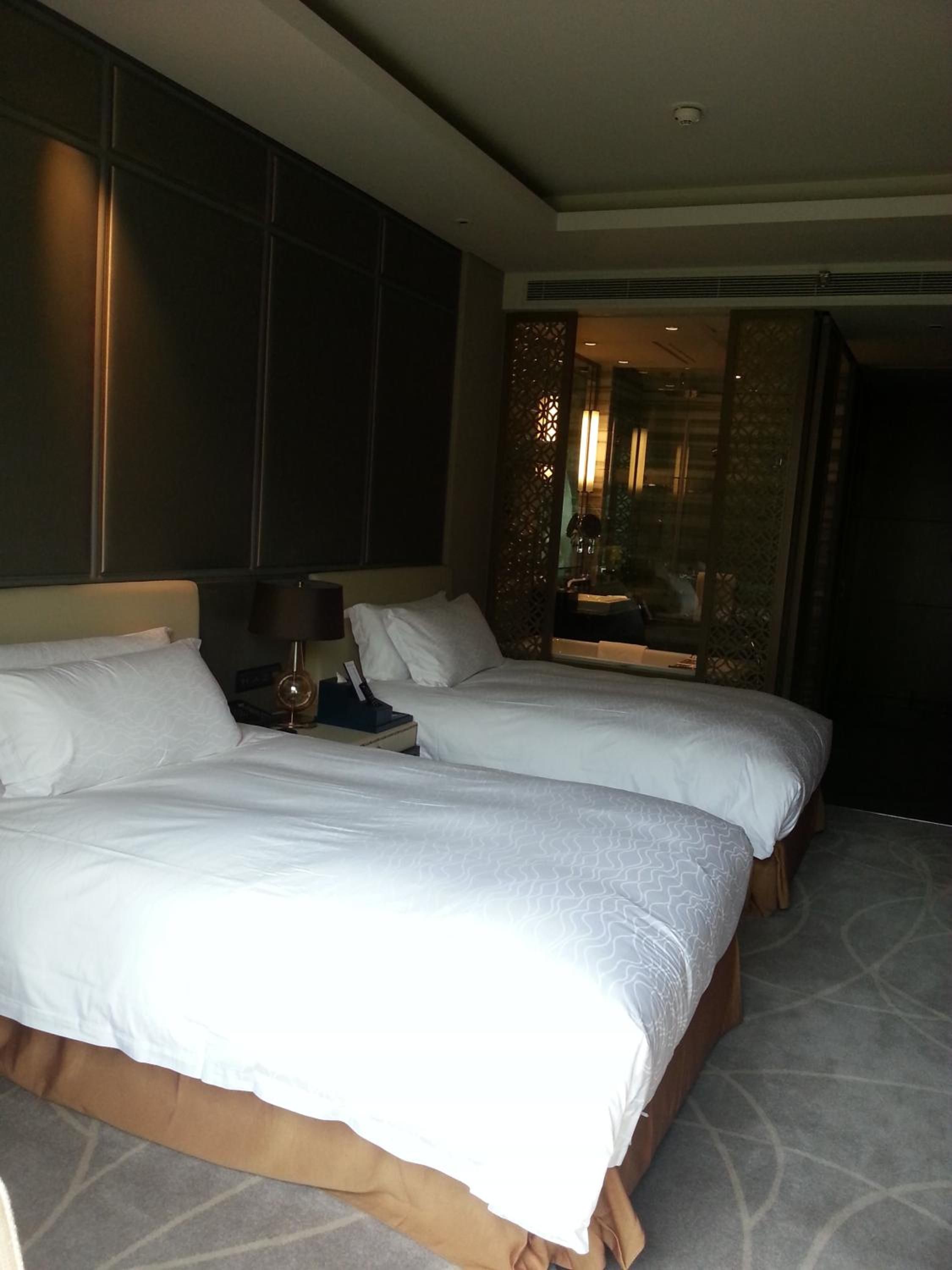 A hotel room with two beds, a large window, and a view of a cityscape.