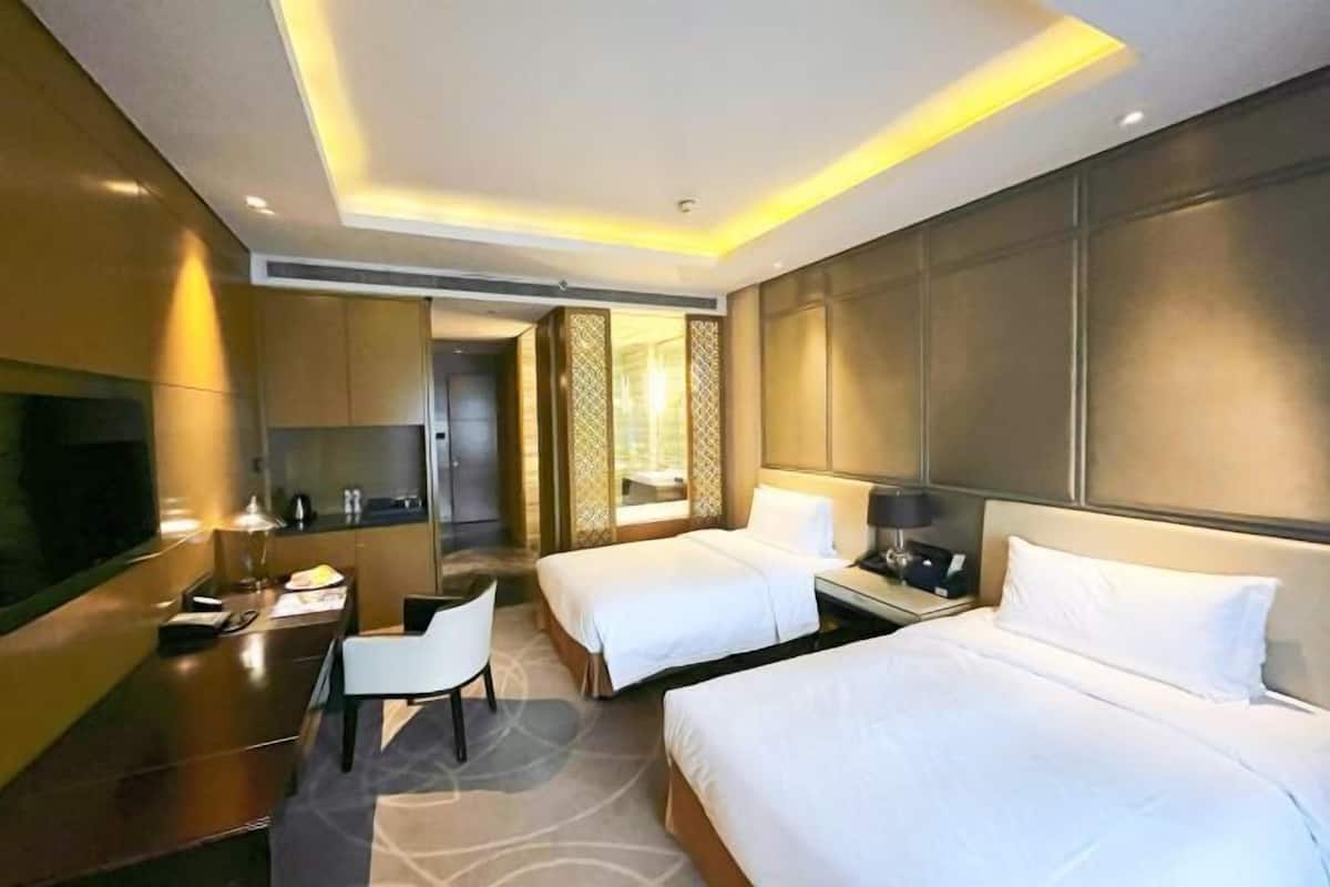 A hotel room with two beds, a desk, a chair, a TV, and a bathroom visible through a door.