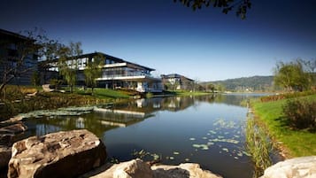 A lakeside view with modern buildings, a calm lake, and surrounding greenery.