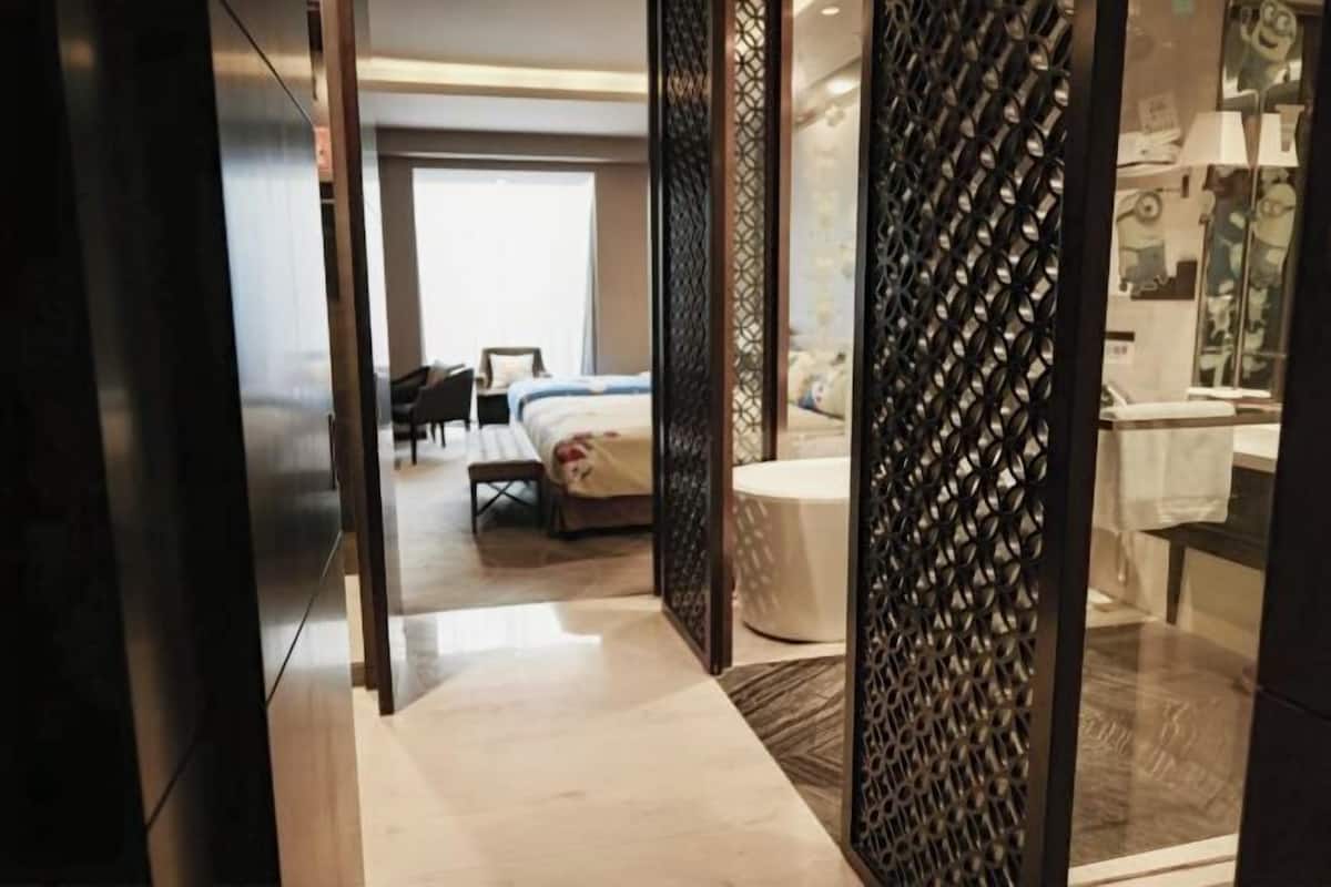 A hotel room with a bed, a desk, a chair, and a bathroom with a sink and mirror.