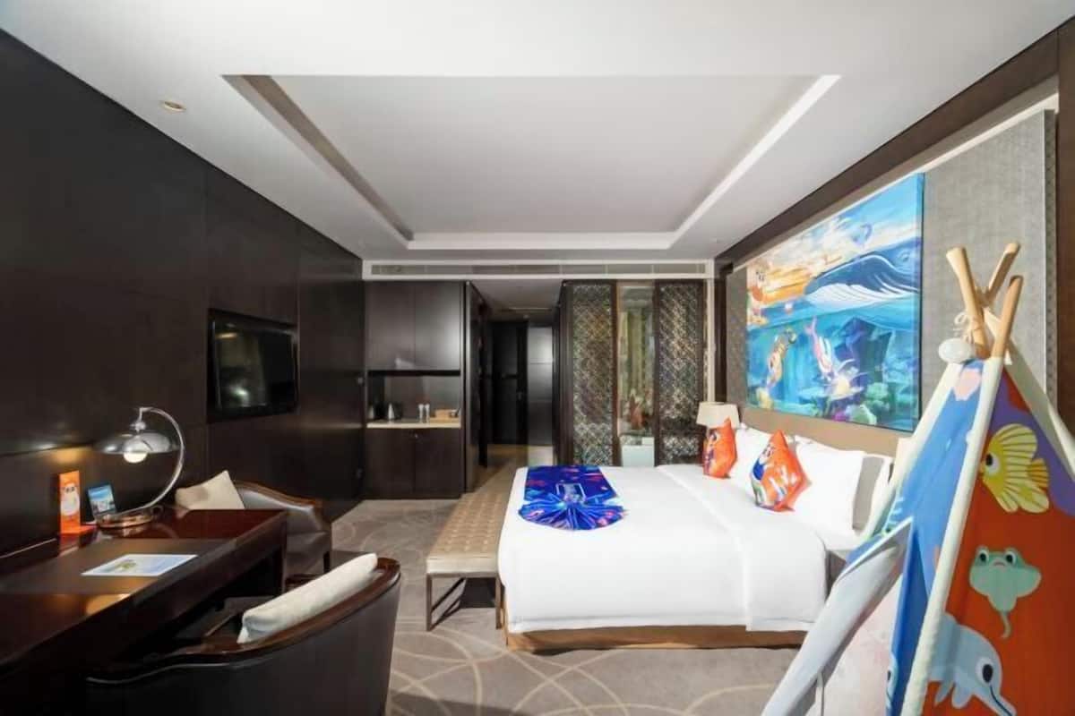 A hotel room with a bed, desk, chair, and a painting on the wall.