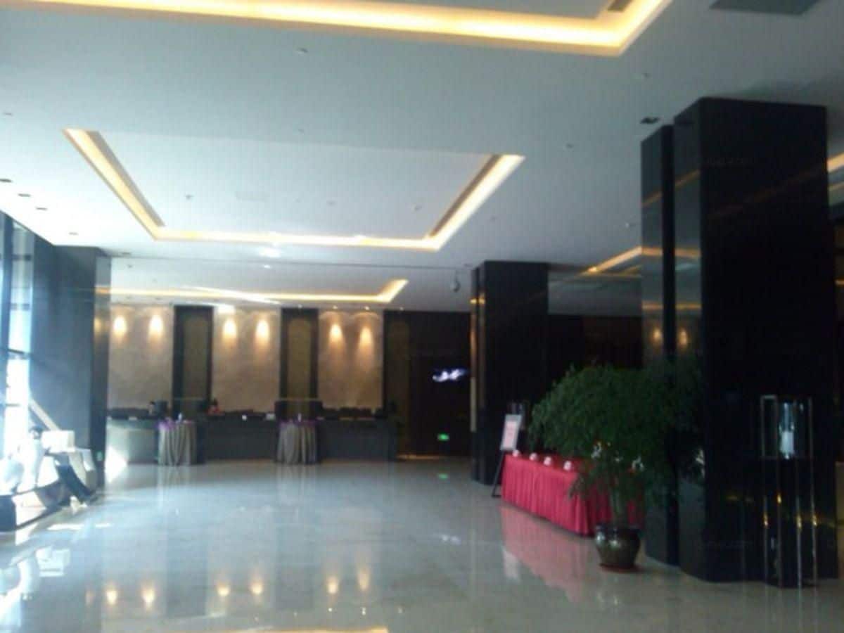 A spacious lobby with a reception desk, a large potted plant, and a modern ceiling design.