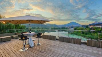 Relax on the deck overlooking the calm water, surrounded by lush greenery and distant mountains.