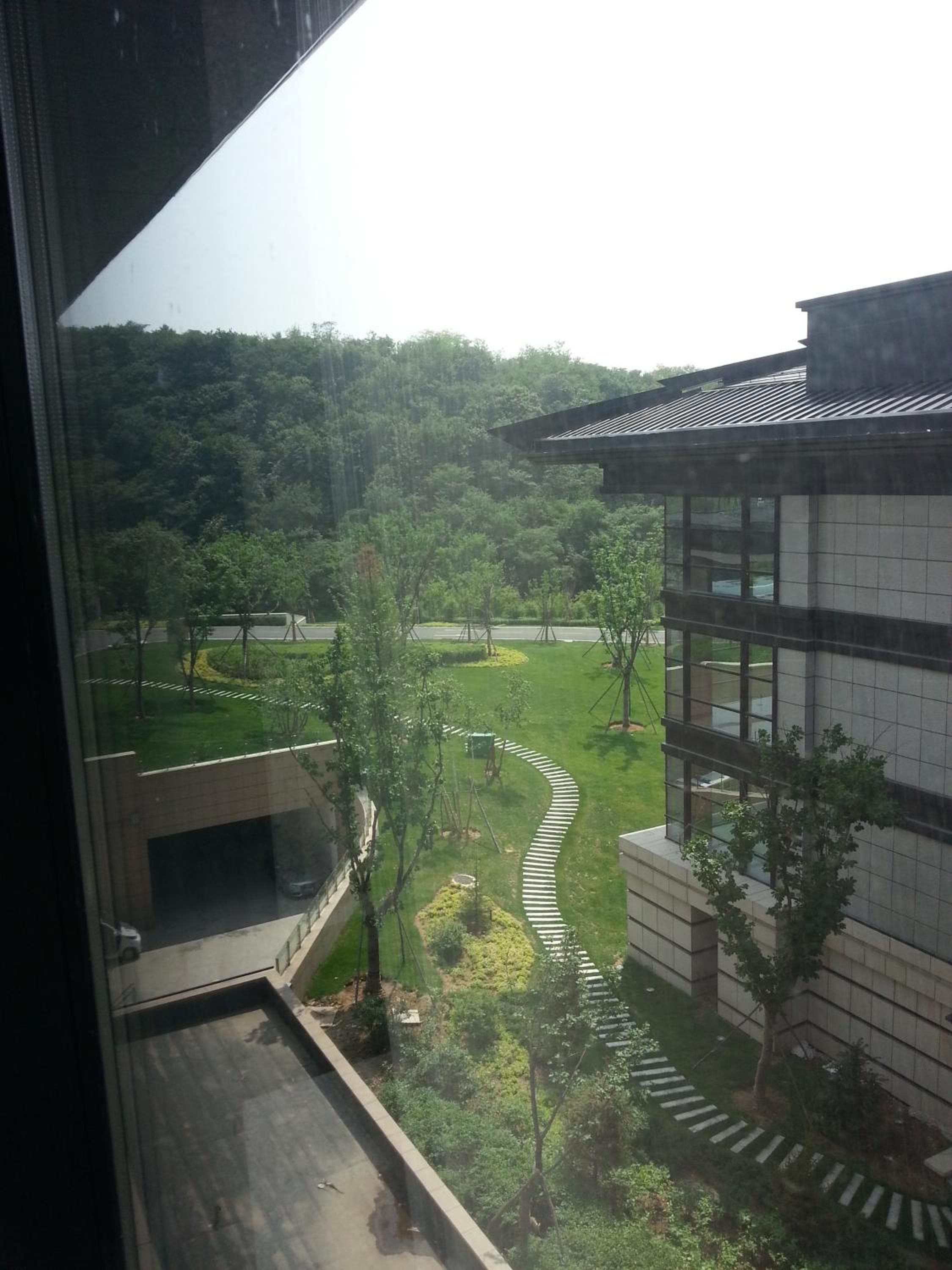 A view of a building with a modern design, surrounded by a well-maintained garden and a forested area in the background.
