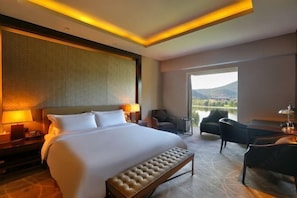 A hotel room with a large bed, bedside lamps, a desk, and a view of a lake.