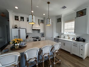 A modern kitchen with white cabinetry, a central island with chairs, pendant lights, and a large window.