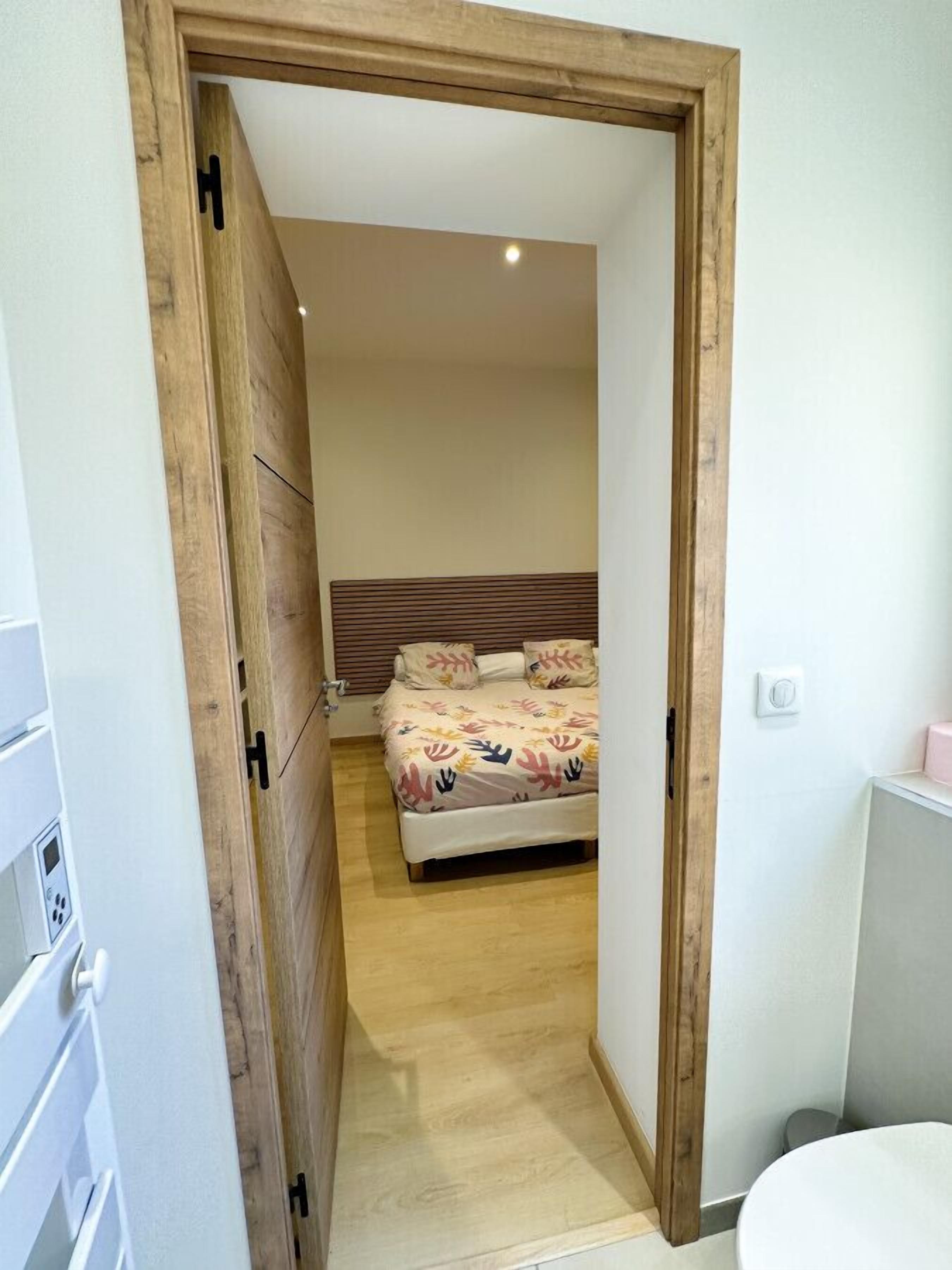 A narrow hallway leading to a bedroom with a bed, wooden headboard, and a white toilet.