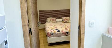 A narrow hallway leading to a bedroom with a bed, wooden headboard, and a white toilet.