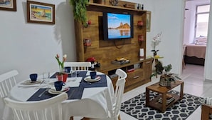 A dining area with a table set for two, a TV mounted on a wooden wall, and a small side table with a plant. - Ap Copacabana 200m da praia – CP1 (Rio de Janeiro)