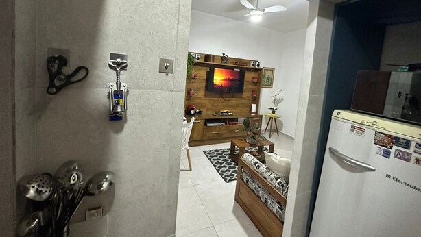A living room with a TV mounted on a wooden wall, a ceiling fan, and a refrigerator with magnets. - Ap Copacabana 200m da praia – CP1 (Rio de Janeiro)