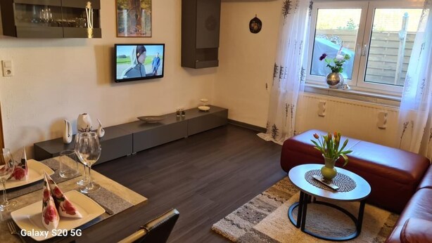 A modern living room with a Galaxy S20 5G, a TV, a sofa, and a dining area with a table set for two. - Vacation apartment Eulennest (Staudernheim)