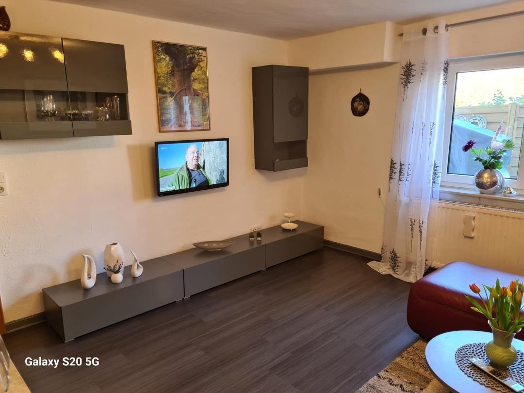 A modern living room with a flat-screen TV, built-in cabinets, and a red ottoman.