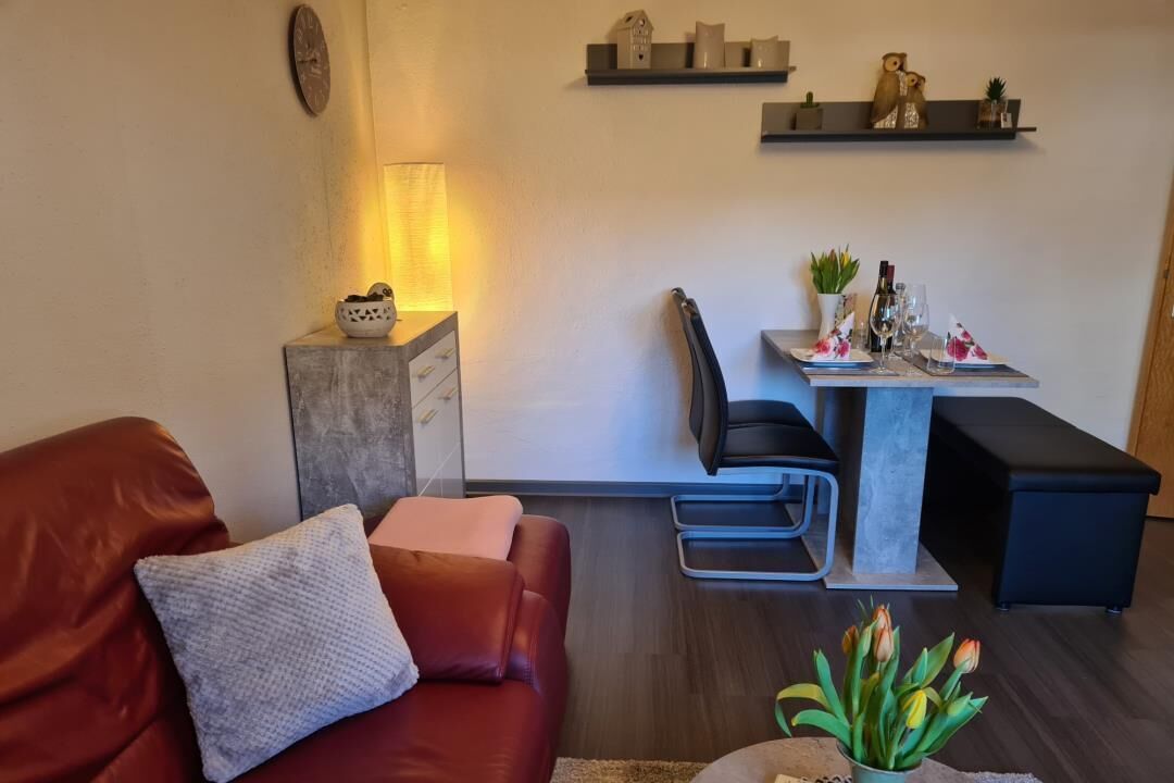 Un salon moderne avec un canapé rouge, une petite table d’appoint, une table basse, une table à manger avec des chaises et un banc noir.