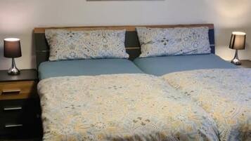 Une chambre à coucher avec un lit, deux lampes de chevet, un luminaire fixé au mur et un tableau encadré au-dessus du lit.