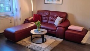 A modern living room with a red leather sofa, a small round coffee table with a vase, and a framed picture on the wall. - Vacation apartment Eulennest (Staudernheim)