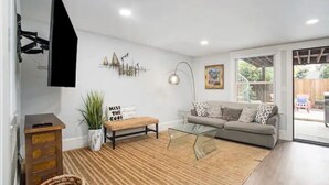 Una sala de estar moderna con sofá, una mesa de centro de vidrio y un televisor montado en la pared.
