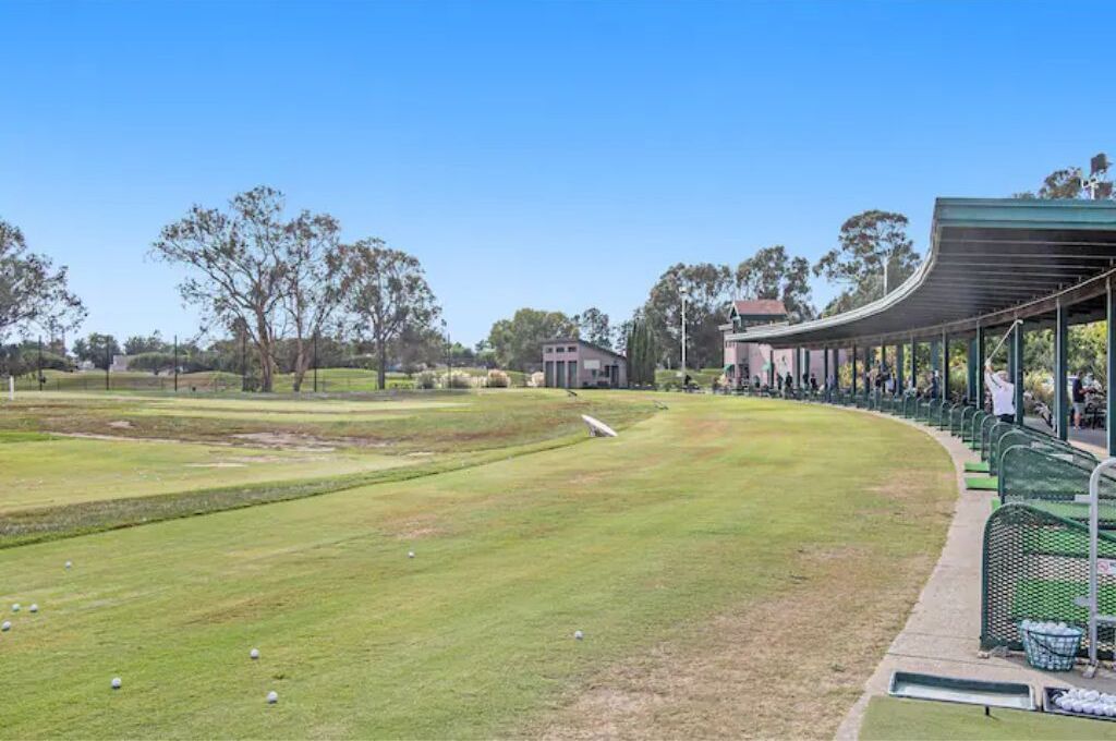 A golf course with a covered seating area and a small building in the background.