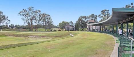 A golf course with a covered seating area and a small building in the background.