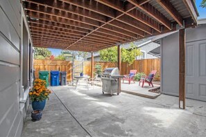 A covered patio area with a grill, outdoor seating, and a wooden fence in the background.