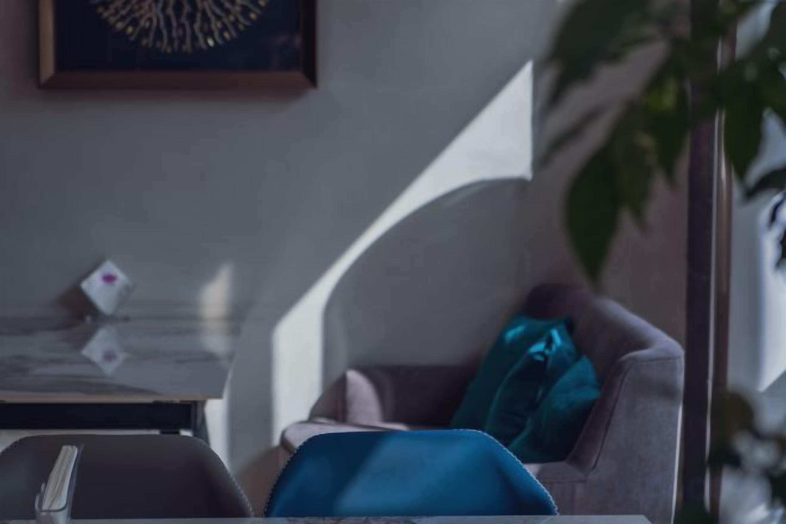 A room with a glass table, a chair with a blue blanket, and a plant.