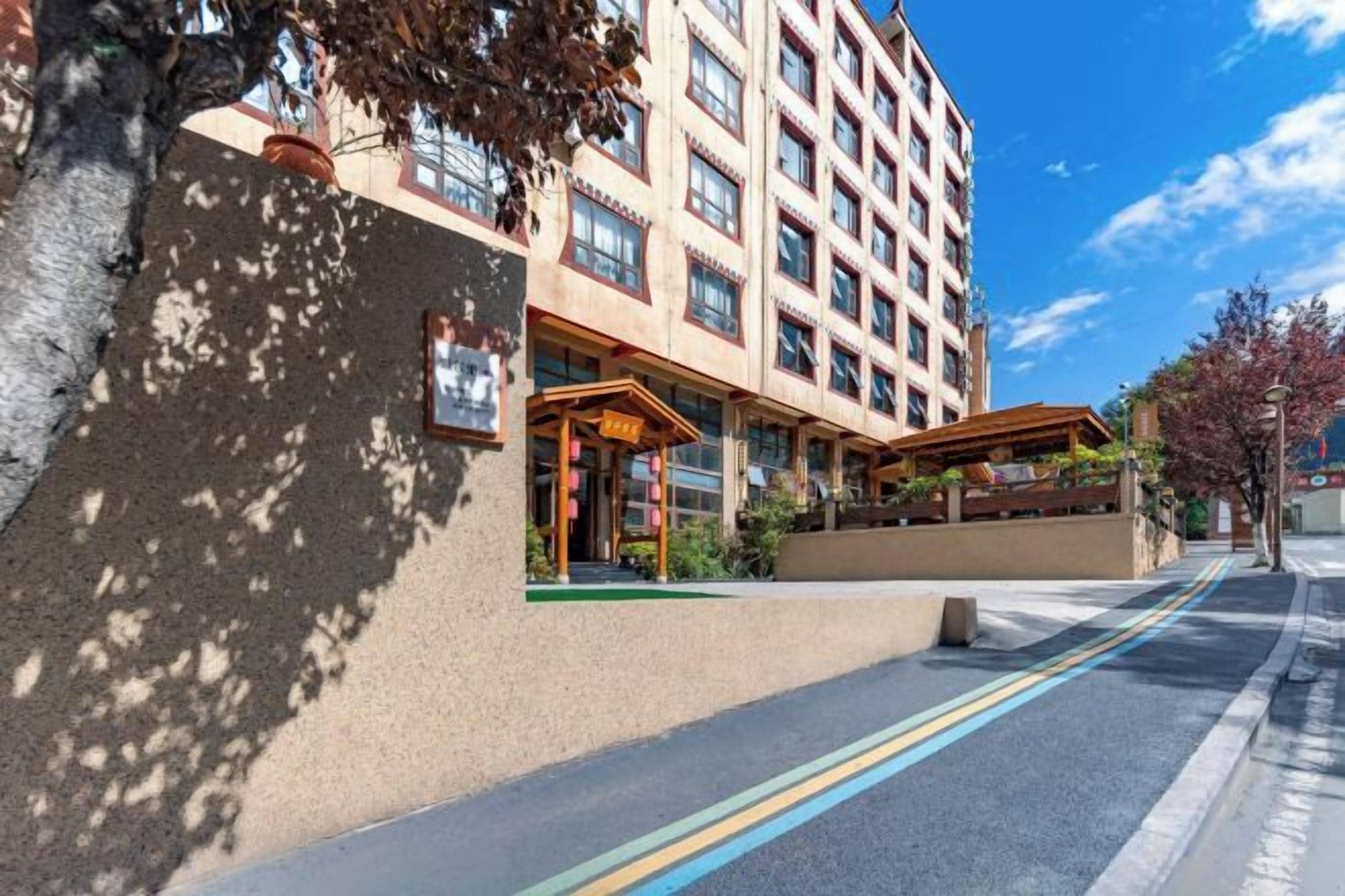 A multi-story hotel with a covered entrance, a paved walkway, and a clear sky.