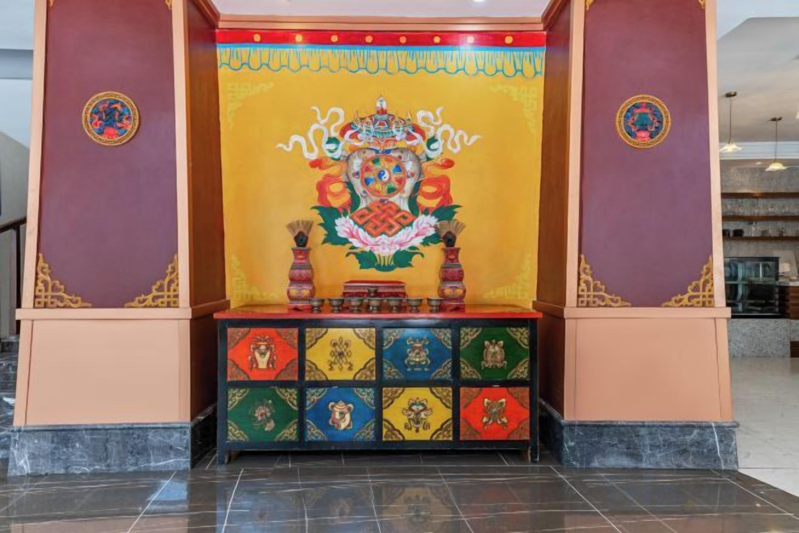 A room with a traditional altar, a prayer wheel, and a colorful tapestry.