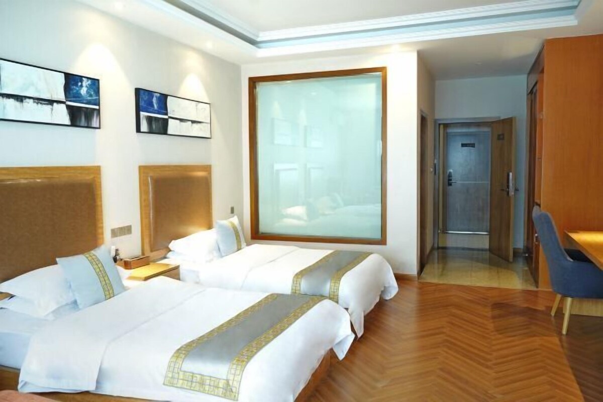 Une chambre d’hôtel avec deux lits, une grande fenêtre, un bureau et une armoire.