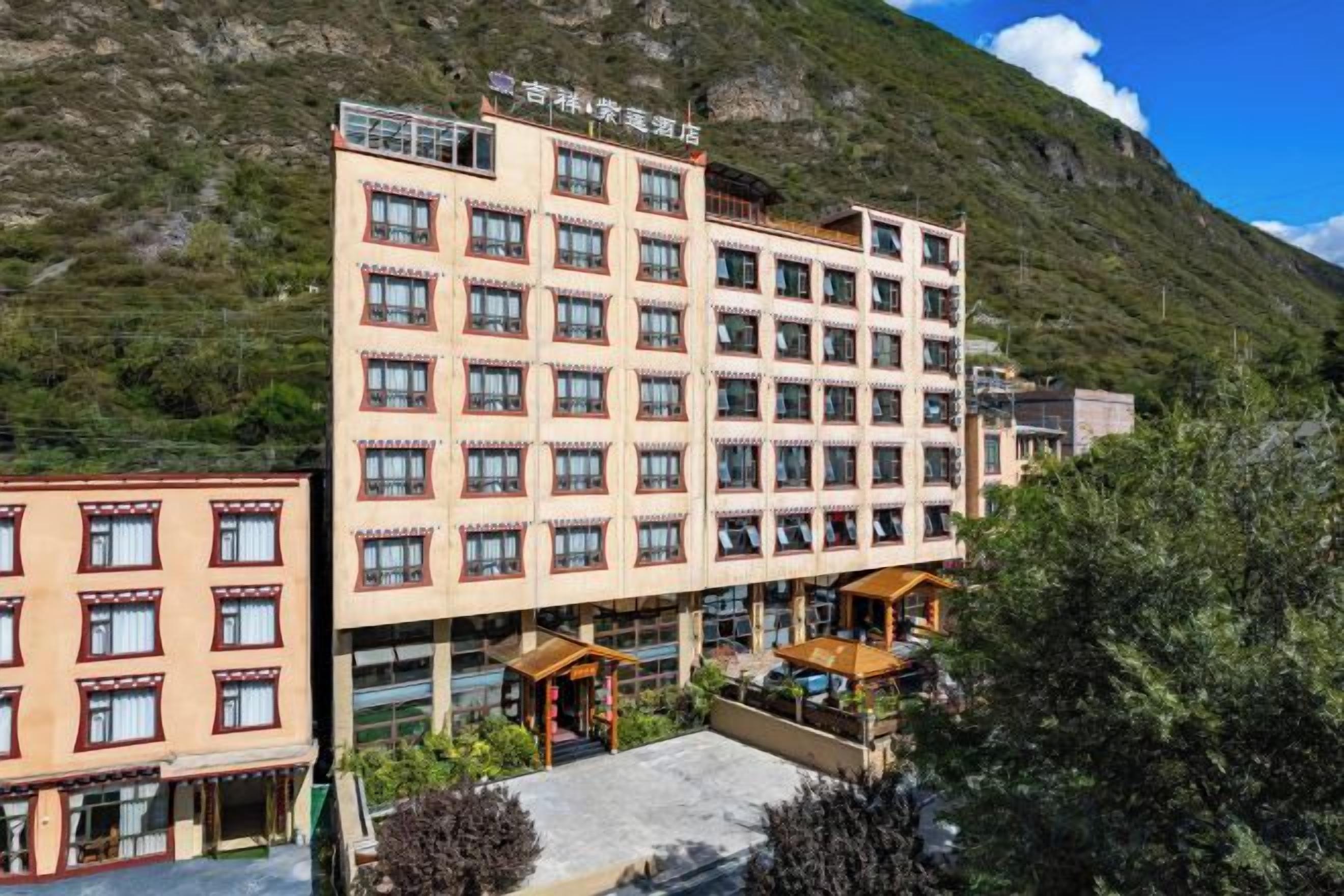 A multi-story hotel with a flat roof, surrounded by greenery and a mountain backdrop.