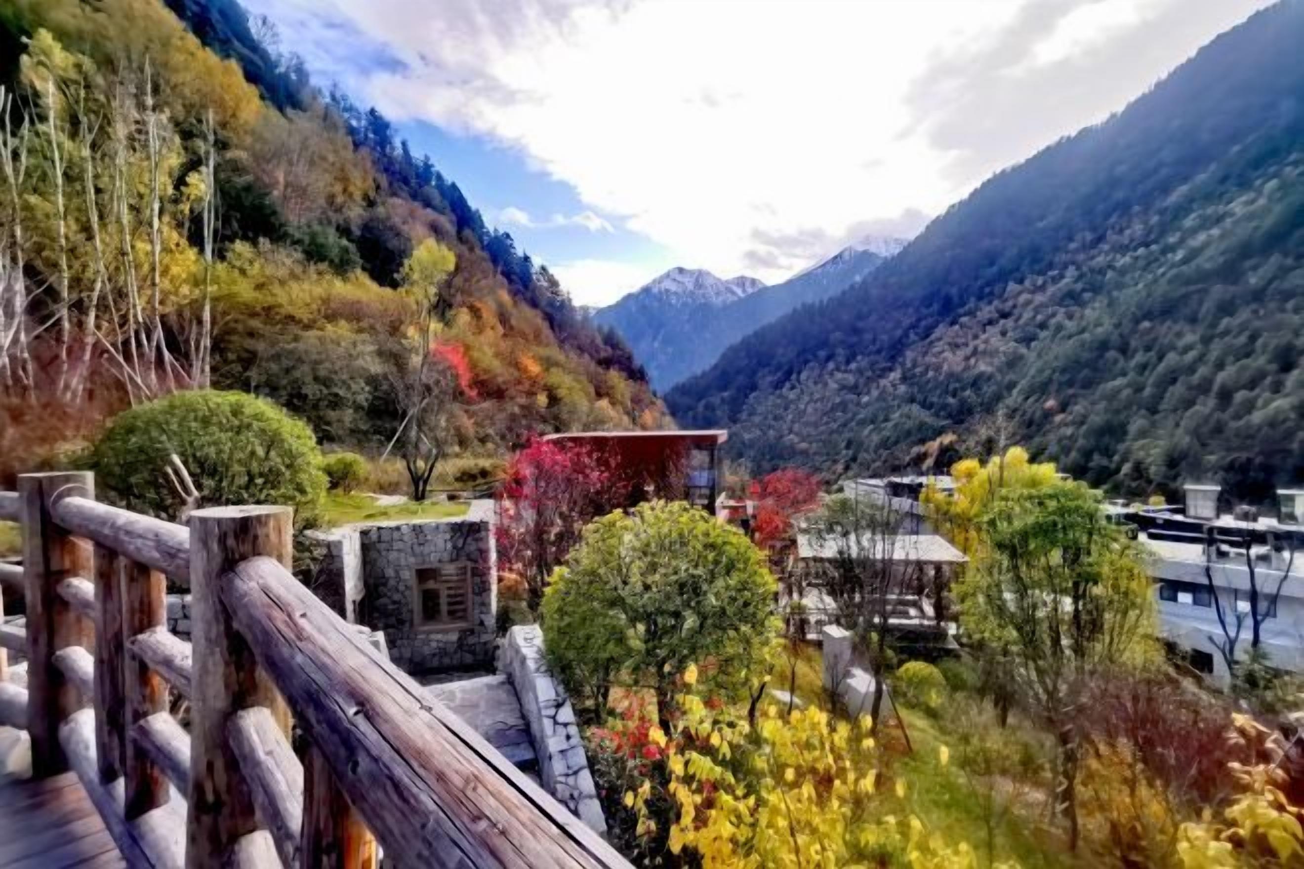 A mountainous landscape with a wooden deck, stone buildings, and a river.
