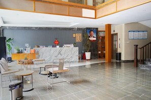Un vestíbulo de hotel con una recepción, zona de estar y una escalera.