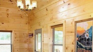 Un comedor rústico de madera con una mesa grande y bancos, una araña y un cartel en la pared.