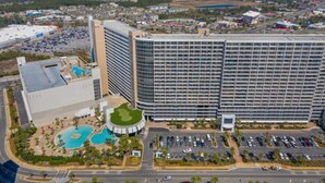 A high-rise hotel with a large pool area, multiple parking lots, and a view of the surrounding cityscape.