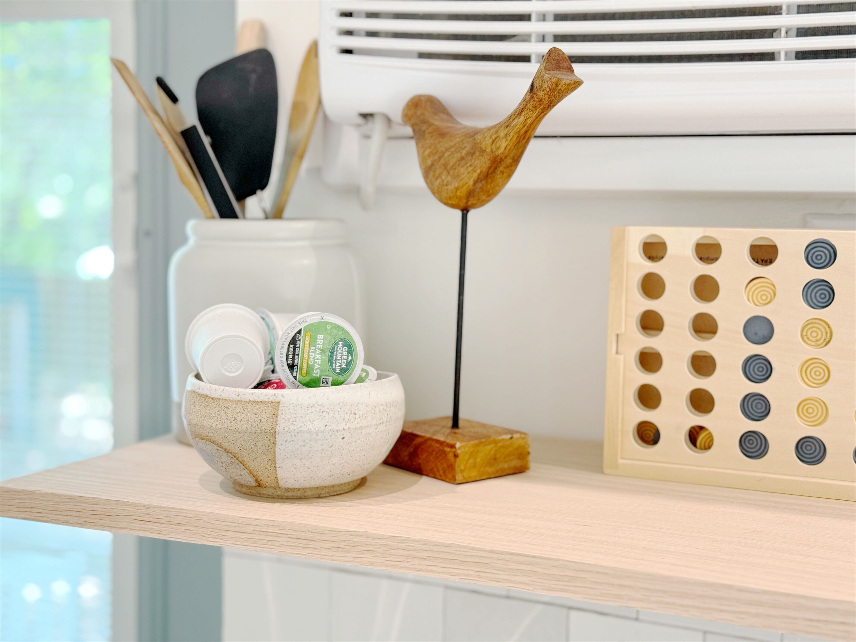 Una encimera de cocina con un bol de cerámica que contiene frascos, un portalápices de madera y una tabla de puzle de madera.