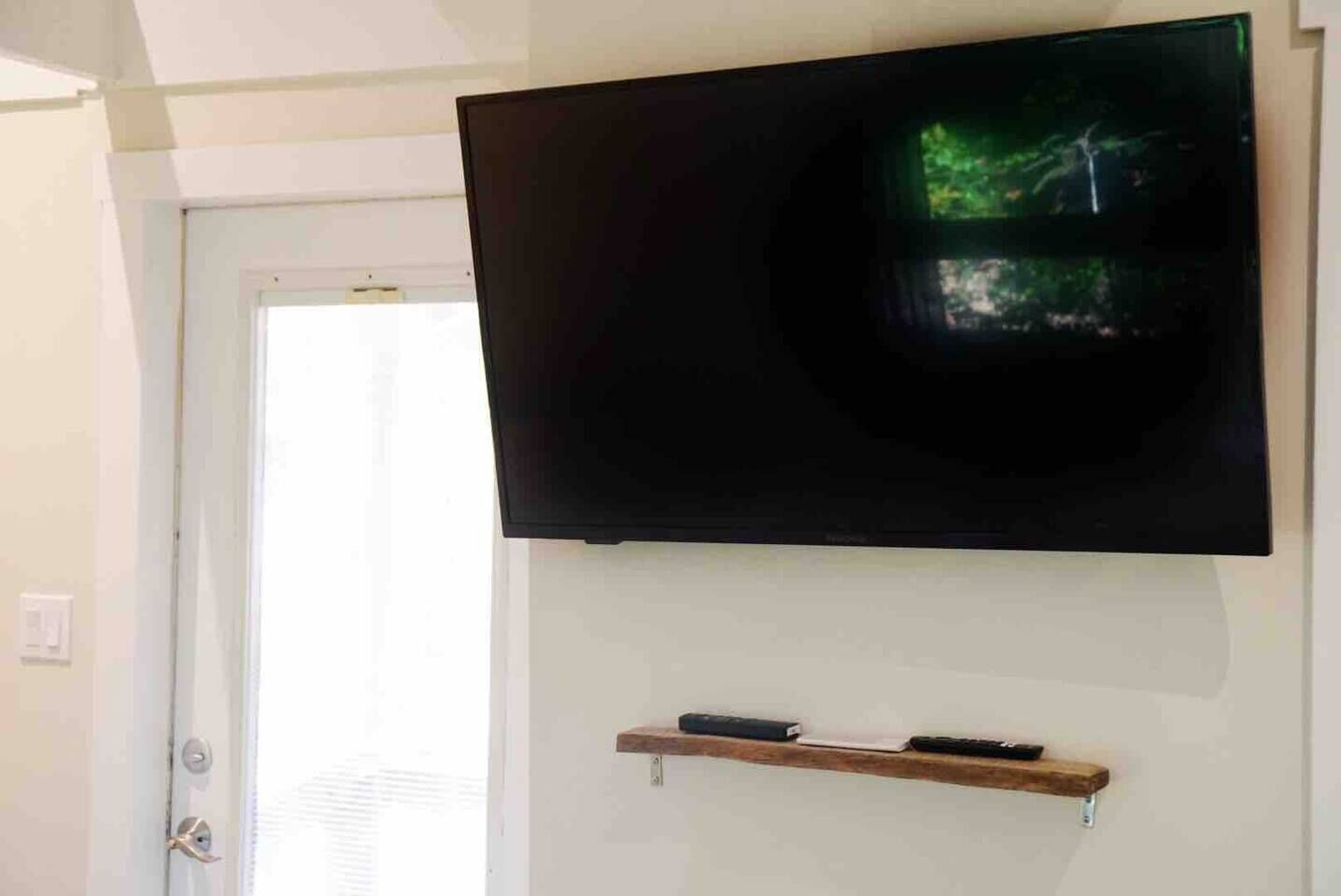 A flat-screen TV mounted on a wall above a wooden shelf with two remote controls.