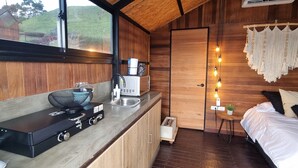 A compact kitchen with a stove, microwave, and sink. There's a window with a view of greenery outside. - Woodside Ecoliving Guatape (Guatapé)