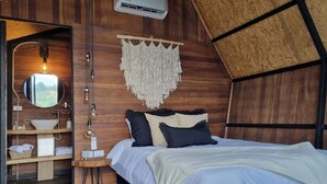 A bedroom with a wooden ceiling, a bed with white bedding, a bedside table with a lamp, and a wall-mounted air conditioner. - Woodside Ecoliving Guatape (Guatapé)