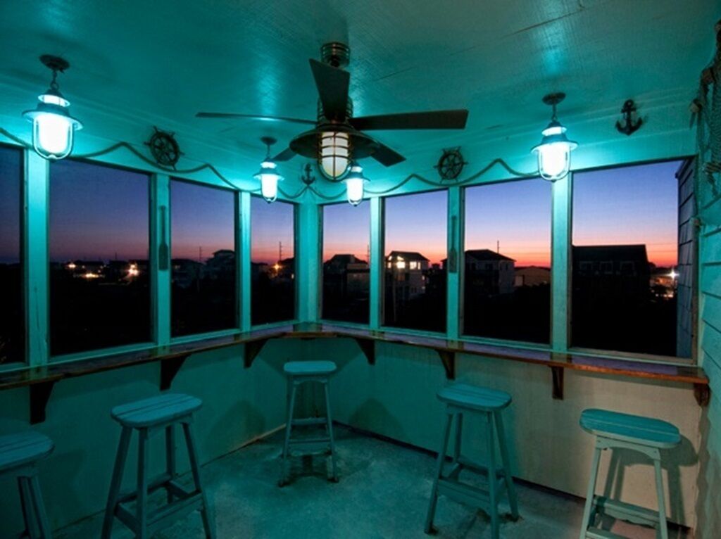 A room with a curved ceiling, large windows, and a ceiling fan. There are three stools and a bar counter.