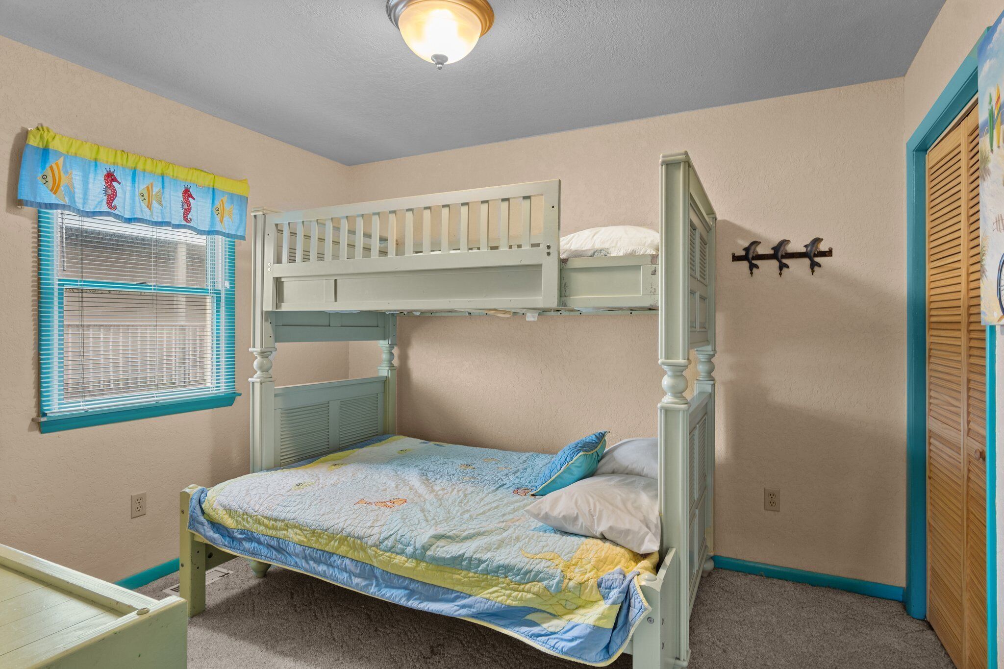 A bunk bed room with a window, a wall-mounted coat rack, and a door with a wooden frame.