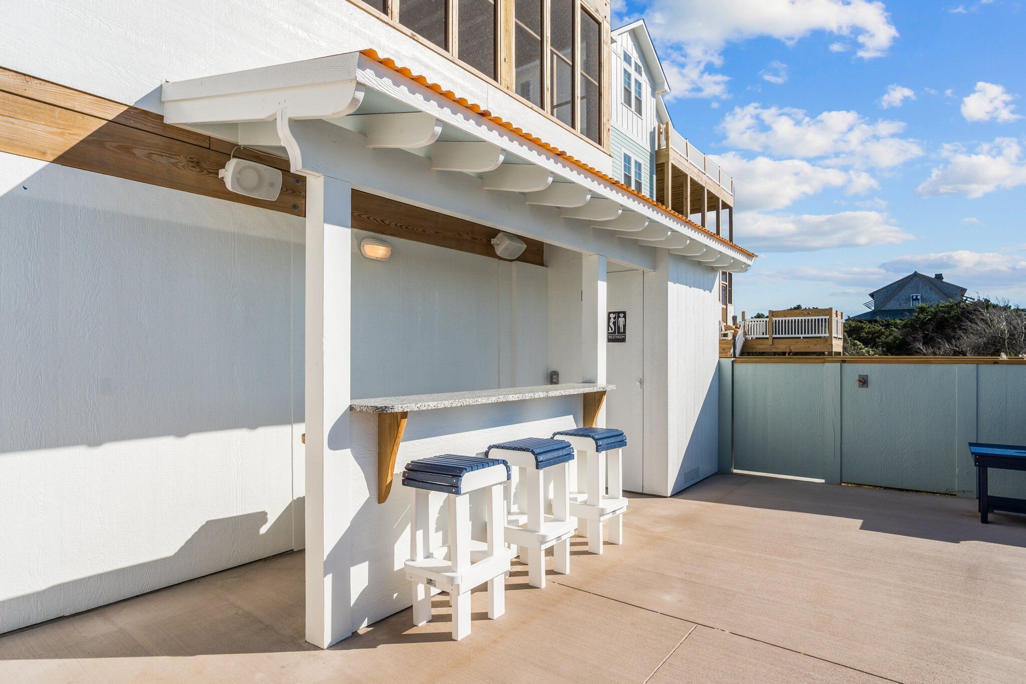 A covered outdoor seating area with a white railing and blue cushioned stools.