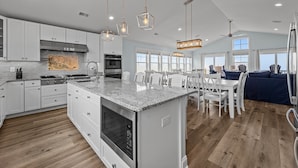 Una cocina amplia con armarios blancos, encimera de granito y horno empotrado. Se observan luces colgantes y un ventilador de techo.