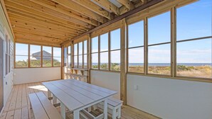 Un espacio al aire libre techado con una mesa y bancos de madera, y amplios ventanales que ofrecen vistas al paisaje.