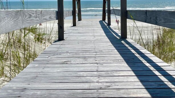 Een houten looppad dat naar het strand leidt, met een helder uitzicht op de zee.