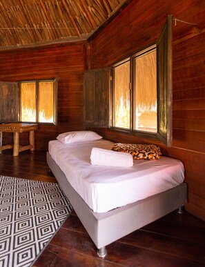 A wooden room with a bed, a table, and a window with a view of trees.