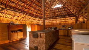 Una cocina rústica con una isla de piedra, armarios de madera y un techo de paja.