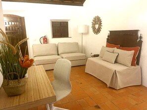 A cozy room with a sofa, a bed with pillows, a lamp, a wall clock, and a door.