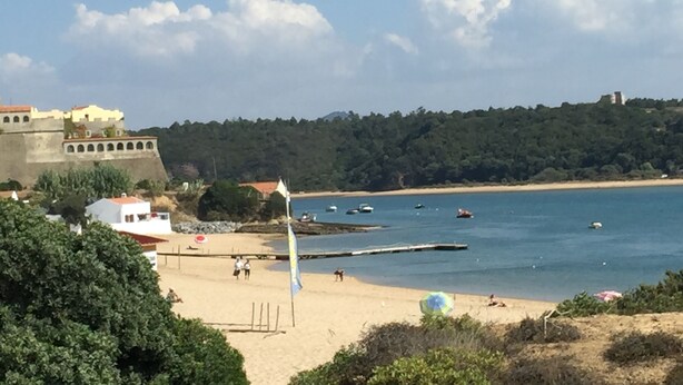 A coastal view with a sandy beach, a flagpole, and a historic building in the background.