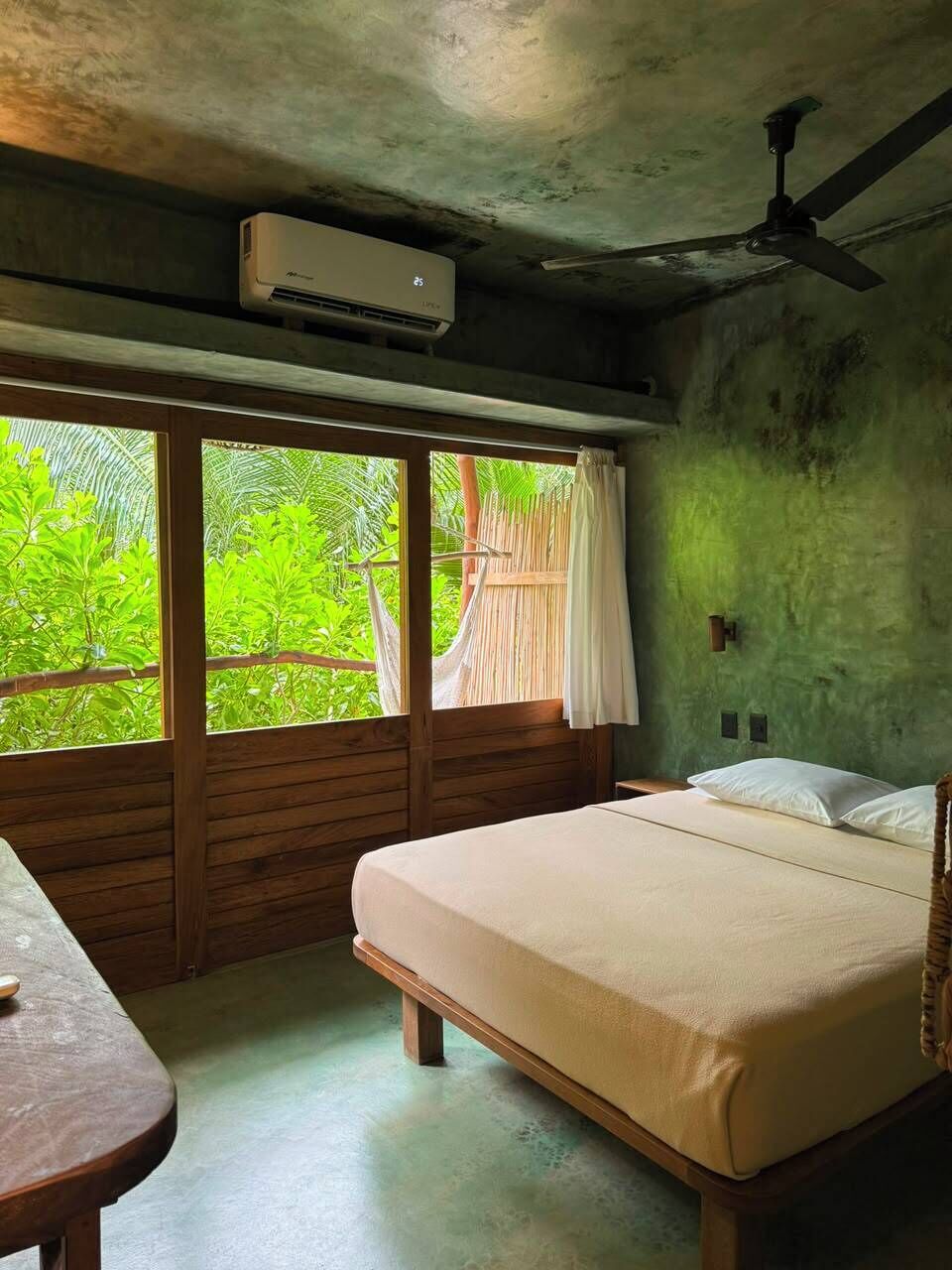 Una habitación con cama, una mesa, ventilador de techo y vistas al exterior.