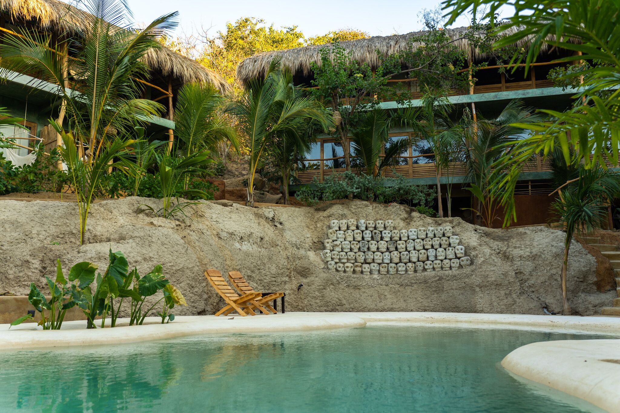 A pool area with a sandy beach, lounge chairs, and a wall of skull decorations.