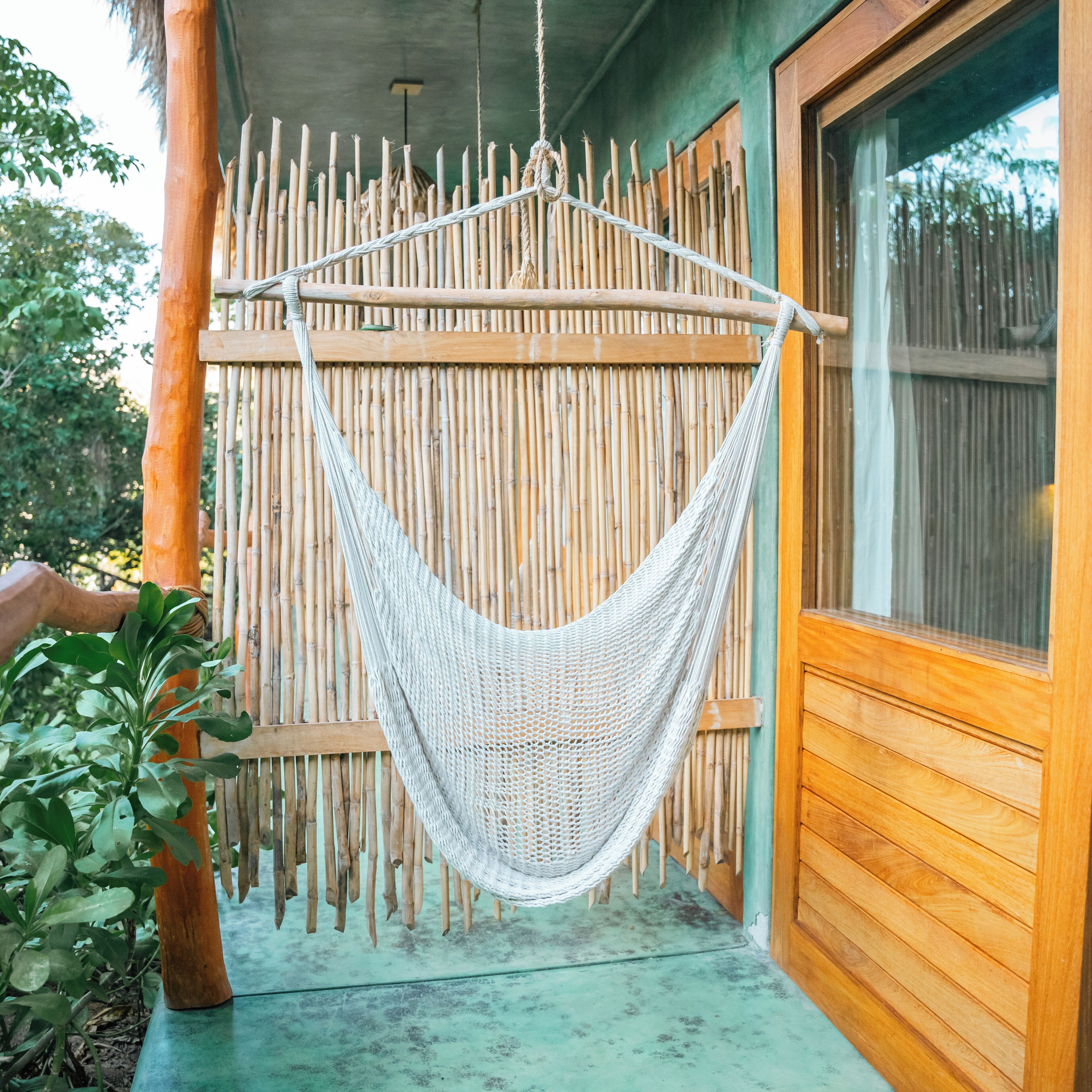 Una hamaca colgada entre una valla de madera y una pared de madera, con suelo de hormigón y una ventana a la derecha.