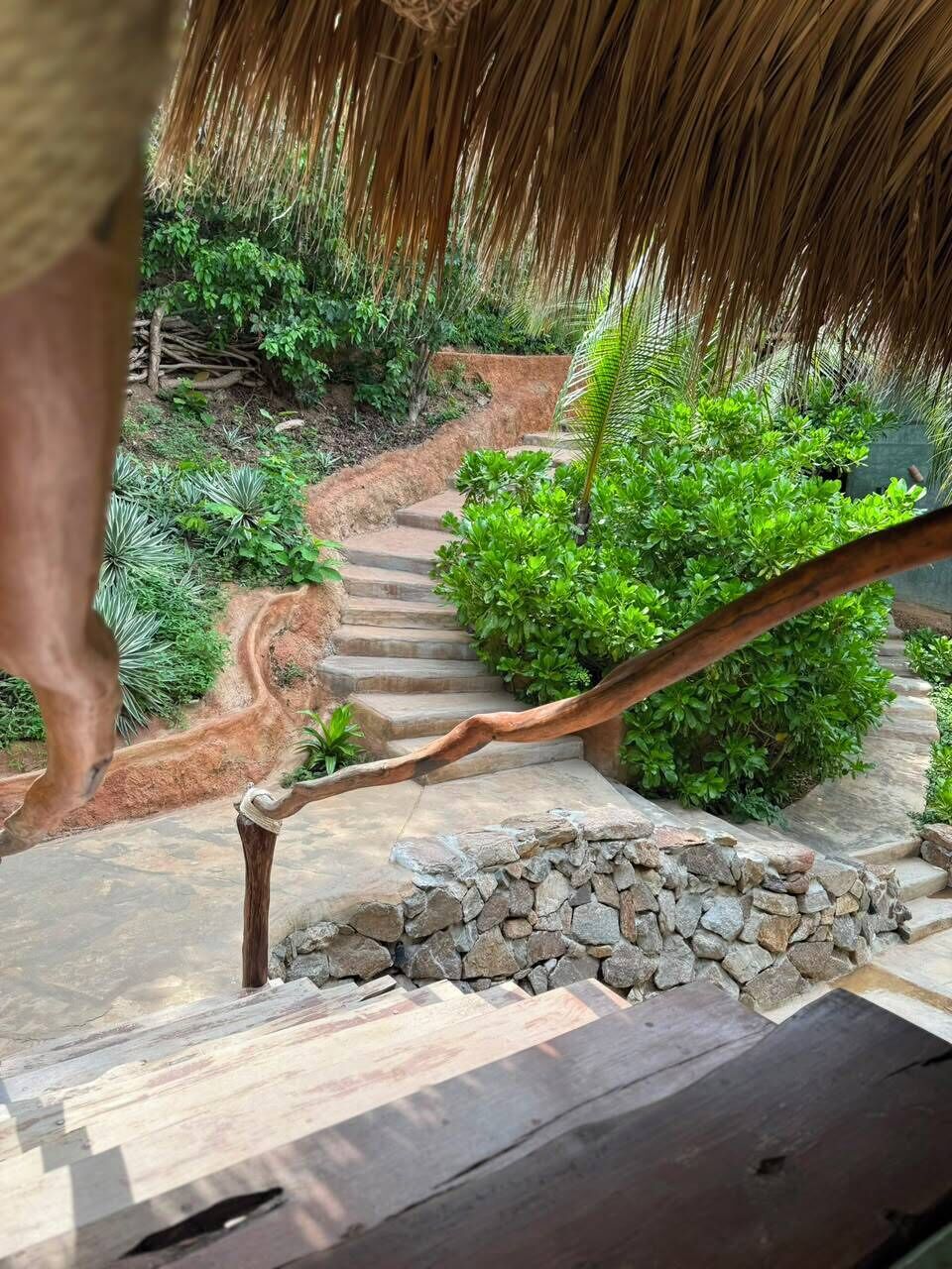 Eine Treppe mit einer Natursteinmauer, umgeben von üppigem Grün und einem hölzernen Geländer.